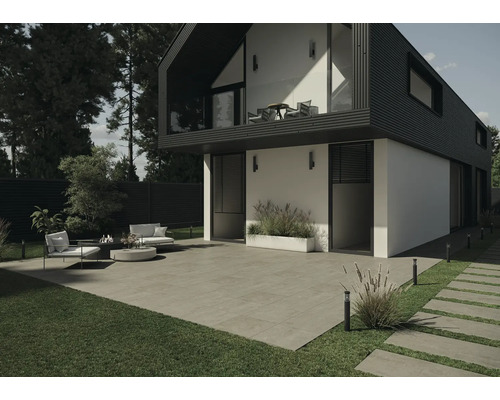 Buitenkant van een modern huis met terrastegels, gazon en tuinmeubilair.