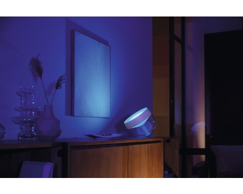 Scene met een nachtkastje met daarop een lamp die blauw licht uitstraalt, een schilderij aan de muur en enkele decoratieve elementen.