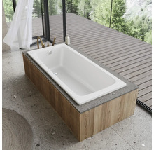 Witte badkuip met houten bekleding voor een raam met uitzicht op bomen