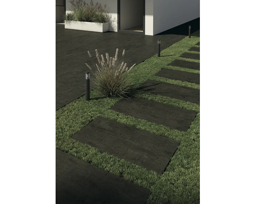 Stenen terrastegels vormen een pad door een tuin, verlicht door tuinlampen.