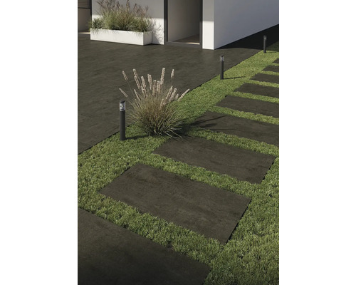 Buitenfoto met terrastegels, gazon en buitenverlichting.