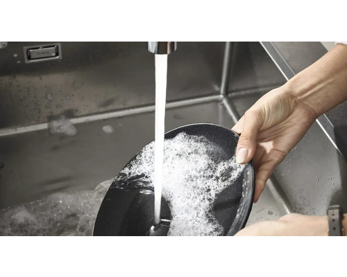 Een persoon spoelt een braadpan af in een gootsteen onder stromend water.