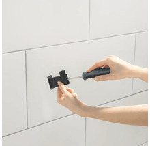 Een persoon bevestigt een zwarte douchehouder met een schroevendraaier aan een witte betegelde wand.