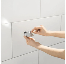 Handen installeren een magnetische deurvanger op een betegelde wand.