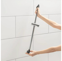 Een persoon houdt een douchestang met verstelbare beugel vast voor een betegelde muur