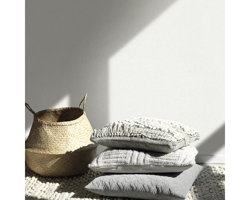 Decoratieve scène met mand en gestapelde kussens op een tapijt.