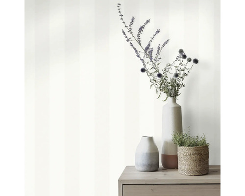 Decoratieve scène met gestreept behang, bloemenvazen en plant in mand op een houten kast