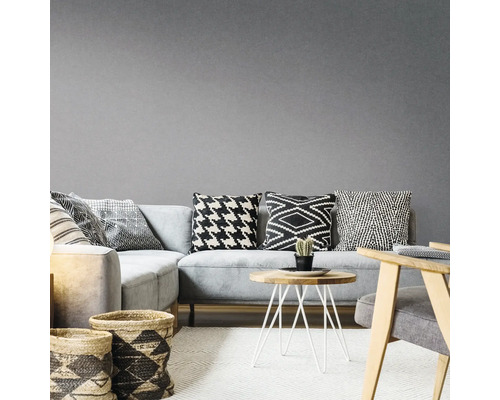 Woonkamer met grijze hoekbank, kussens met patroon, houten tafel en gevlochten manden op een tapijt
