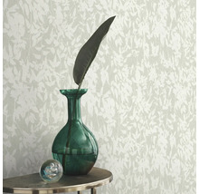 Behang met bladerpatroon, gecombineerd met groene glazen vaas en decoratieve glazen bol op een tafel.