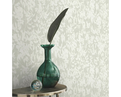 Behang met bladerpatroon, gecombineerd met groene glazen vaas en decoratieve glazen bol op een tafel.