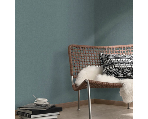 Woonkamer scène met rotan stoel, kussen en patroonbehang.