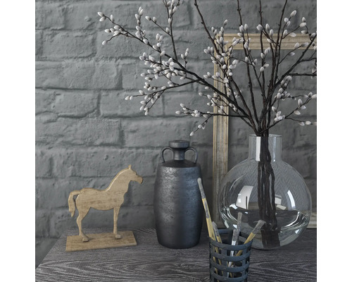 Decoratieve scène met vaas, takken, paardenfiguur en bak met penselen op een tafel voor een bakstenen muur