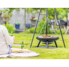 Driepoot barbecue in de tuin met persoon op de achtergrond