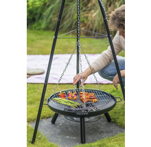 Persoon grilt op een driepootbarbecue met een grillrooster waaraan een ketting is bevestigd. Op het rooster liggen spiesjes, vlees en groene asperges.