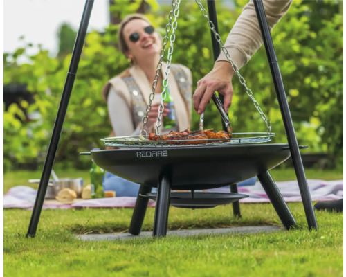 Persoon grilt vlees op een driepootgrill in de tuin