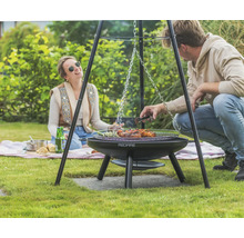 Scene met een Redfire driepoot barbecue in de tuin met twee personen die eten aan het grillen zijn.