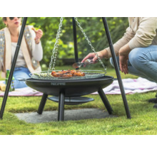 Drie personen barbecueën op een driepootbarbecue in de tuin met vlees en groenten.
