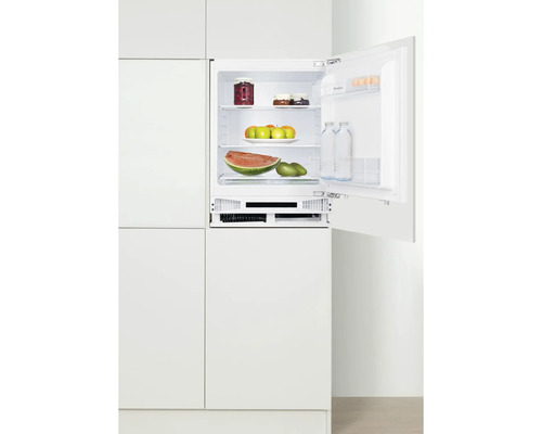 Geopende inbouwkoelkast gevuld met voedsel in een witte keuken.