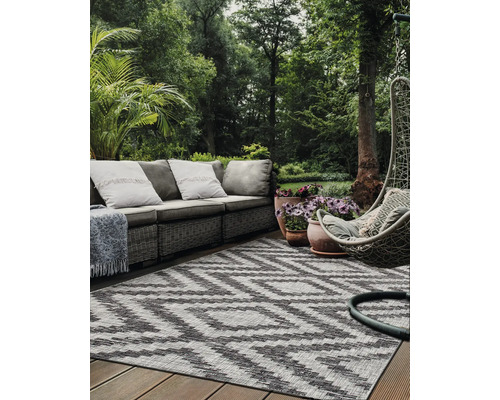 Scene van een terras met een grijze rotan bank, een grijze hangstoel en een buitentapijt met zigzagpatroon.