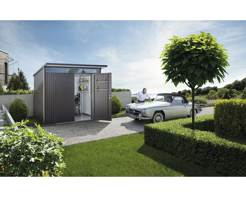 Ruime metalen gereedschapsschuur met open deur in een tuin en man poetst oldtimer