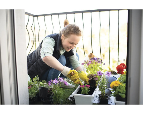Vrouw plant bloemen op een balkon met diverse bloemen en plantenbakken.