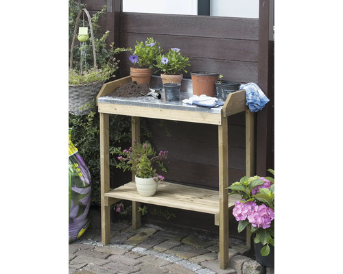 Tuinscene met een houten plantentafel met metalen werkblad, plantenbakken en tuingereedschap.