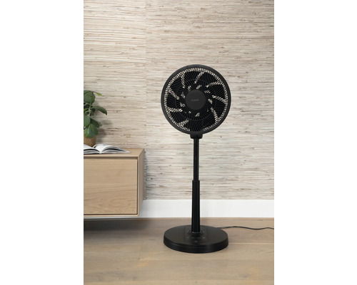 Zwarte ventilator op een houten vloer voor een wand met patroon