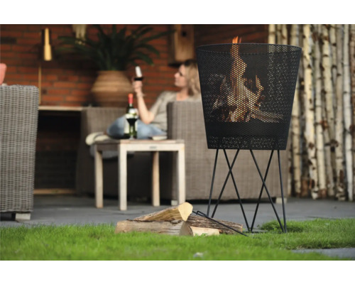 Metalen vuurkorf met brandend hout in een tuinomgeving.
