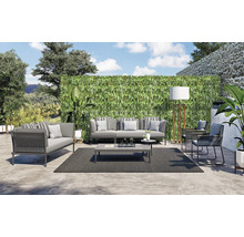 Een loungeset met bank, fauteuil, salontafel en tapijt buiten voor een groene wand.