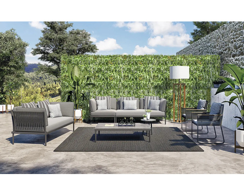 Een loungeset met bank, fauteuil, salontafel en tapijt buiten voor een groene wand.