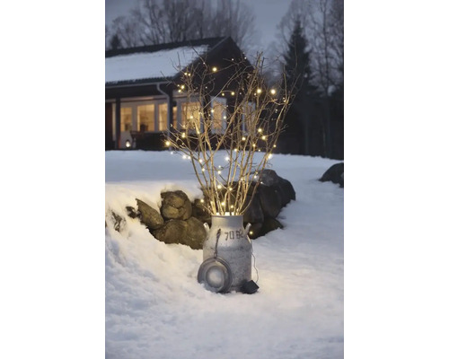 Decoratieve takken met lichtsnoer in een melkkan in de sneeuw