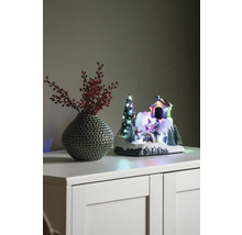 Decoratief winterlandschap met huis, kerstboom en schaatsers naast een vaas met rode bessen op een kast