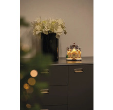 Decoratieve scène met vaas met kunstbloemen en verlicht peperkoekhuis op een commode.