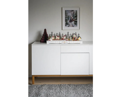 Decoratieve kerstscène met huizen, bomen en trein op een wit dressoir.