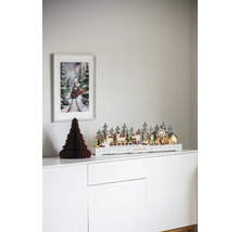 Decoratief kerstdorp met trein op een witte commode met een afbeelding van een trein aan de muur.