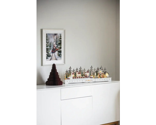 Decoratief kerstdorp met trein op een witte commode met een afbeelding van een trein aan de muur.