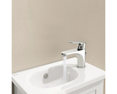 Wastafelkraan van chroom met water uit de kraan op een witte wastafel