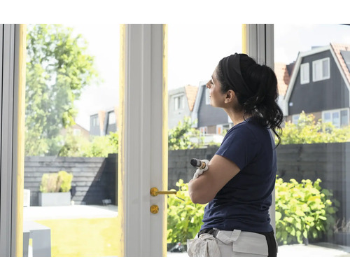 Een vrouw met een kwast staat voor een terrasdeur en kijkt naar buiten.
