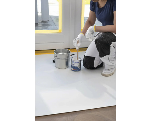 Iemand mengt lakverf in een blik met een houten stok, naast een metalen emmer.