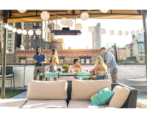 Een groep mensen verzamelt zich op een dakterras onder een terrasverwarmer en een lichtsnoer.