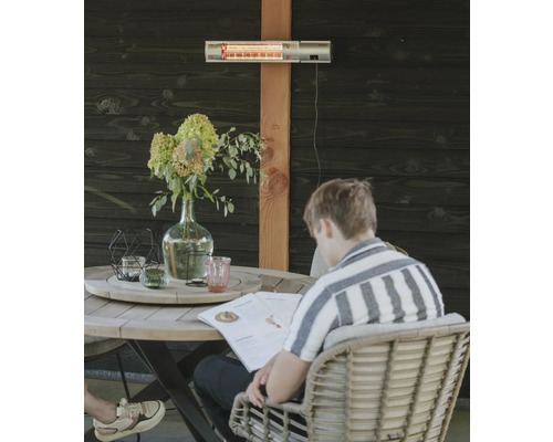 Terras met terrasverwarmer aan houten wand en persoon aan tafel