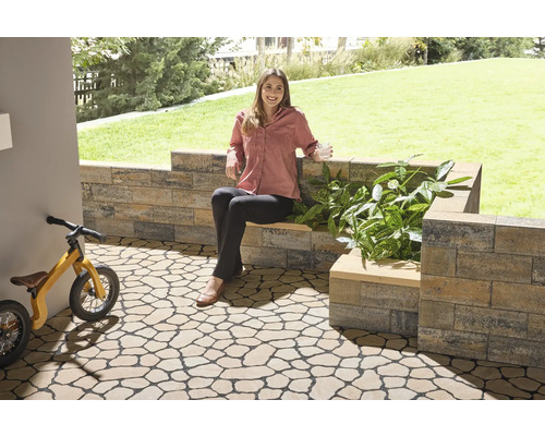 Tuin met vloertegels in natuursteenlook, muur en een vrouw die op een bank zit