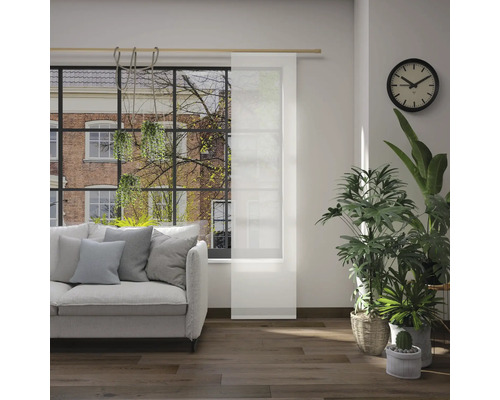 Woonkamer met bank, kamerplanten, klok en schuifpaneel voor het raam