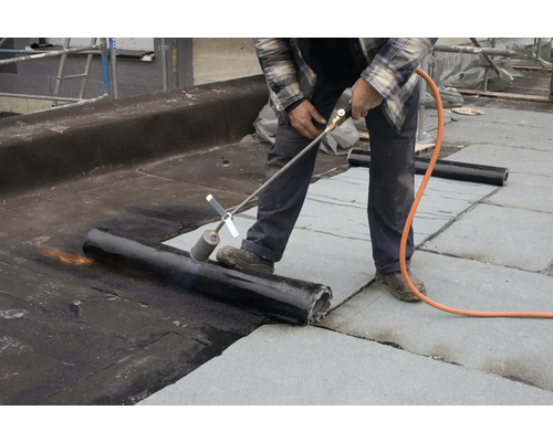 Een man last dakbedekking met een brander op een dak.