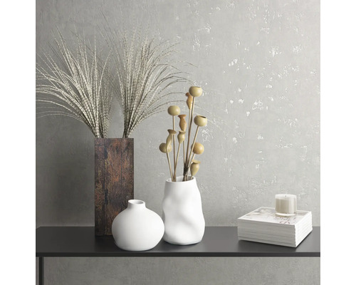 Decoratief stilleven met vazen, sierplanten, kaars en boek op een tafel.