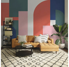 Woonkamer met bruine bank, salontafel, rek en kamerplant voor een muur met geometrisch patroon