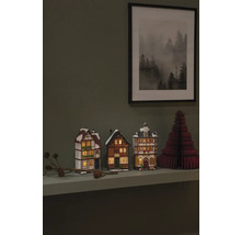 Decoratieve miniatuurhuisjes en een papieren kerstboom op een plank met een ingelijste foto aan de muur