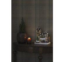 Decoratieve kerstscène met verlicht huis, kaars en plant op een tafel