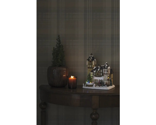 Decoratieve kerstscène met verlicht huis, kaars en plant op een tafel