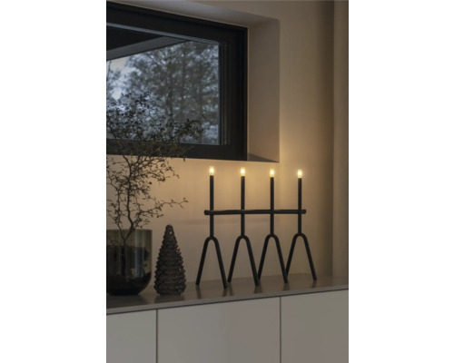 Decoratief arrangement met een zwarte lamp met vier lichten, een kleine spar en een decoratieve tak in een interieur.